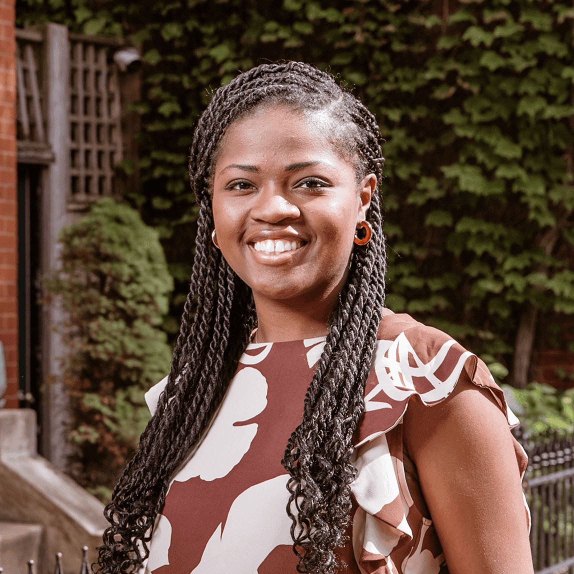 Portrait of Jami Cox Antwi smiling, in front of an ivy-covered wall