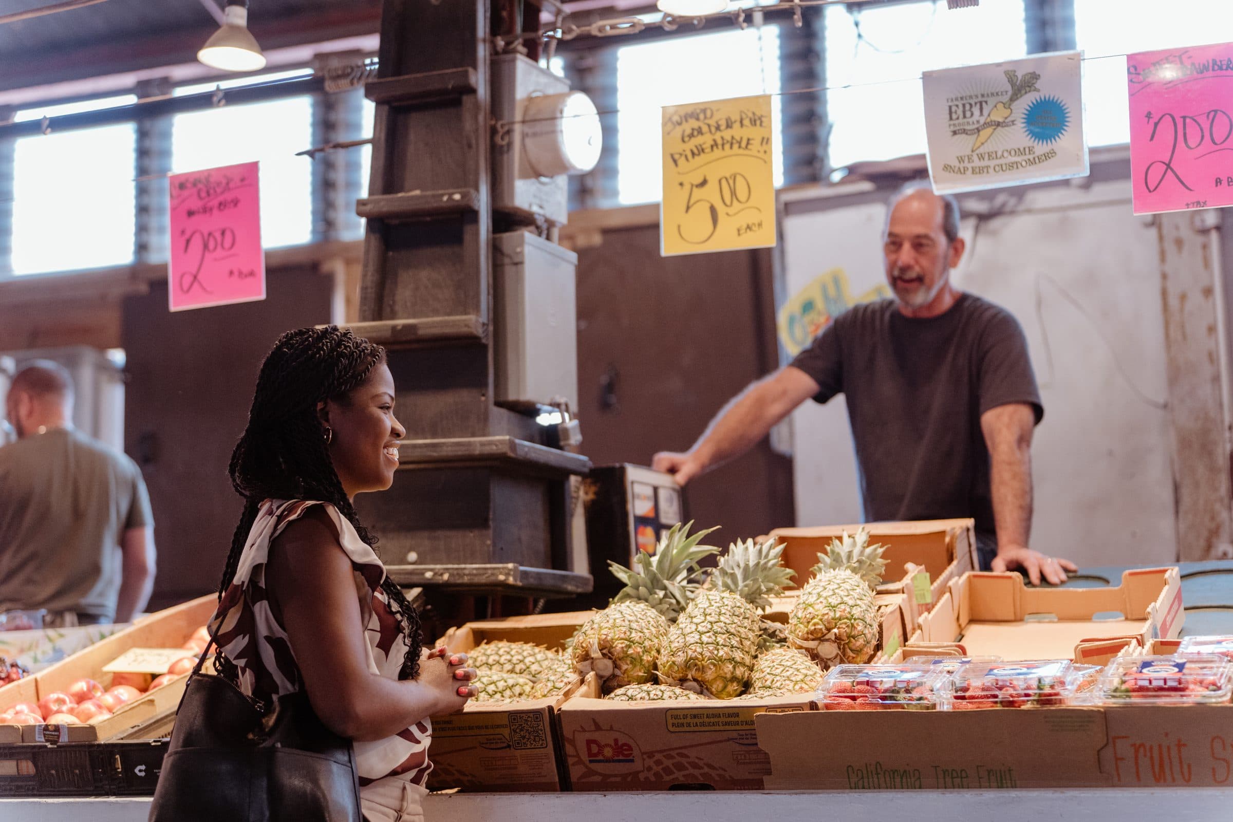 Jami Cox Antwi chatting with a market vendor across a table of fresh pineapples