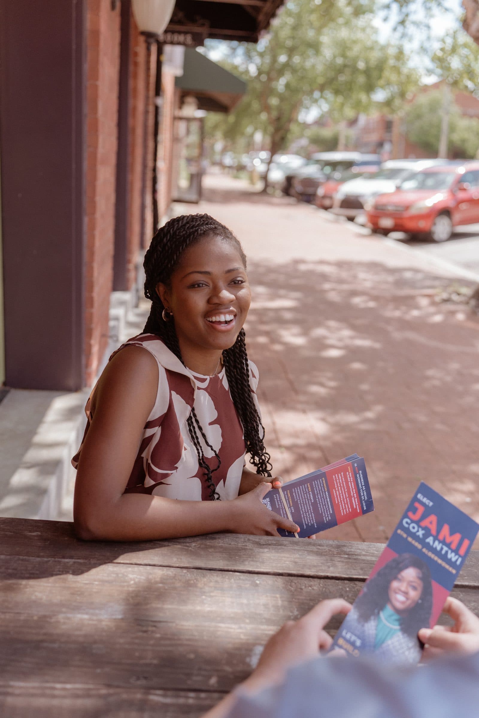 Jami Cox Antwi seated at an outdoor table, sharing campaign literature with a neighbor